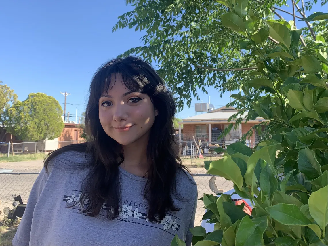 Dark haired woman sits outside under trees, smiling