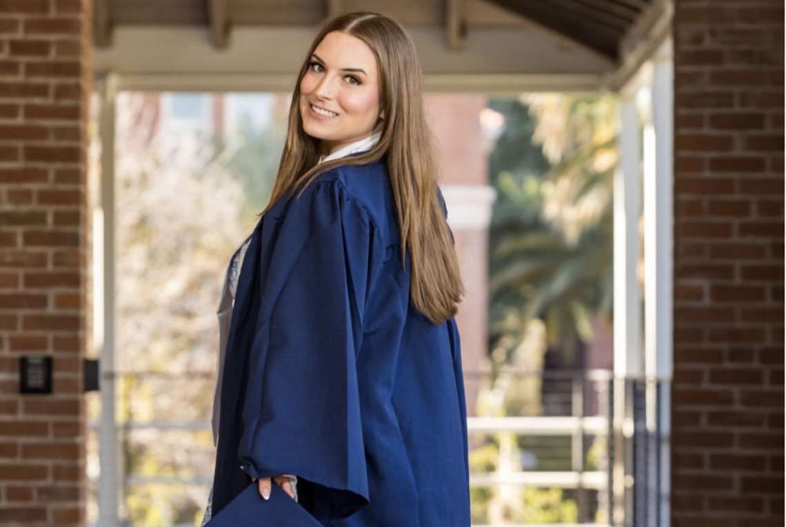 Woman with long hair standing outside in a blue graduation gown