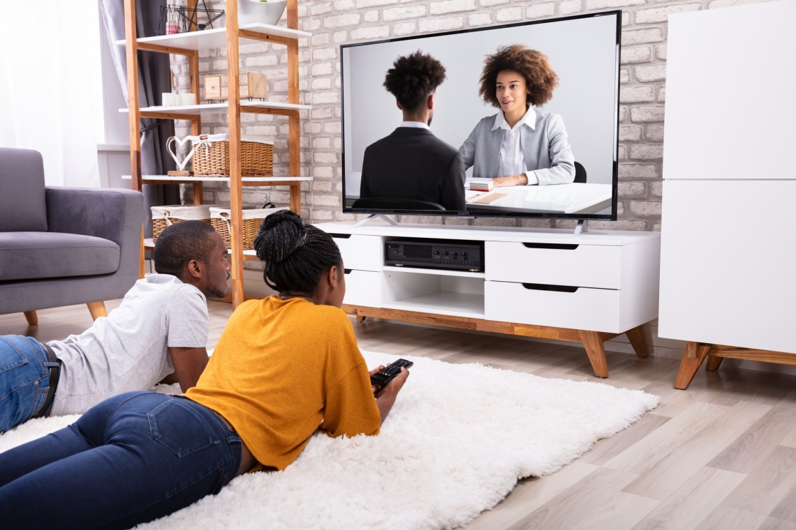 two Black young adults watching TV with Black representation