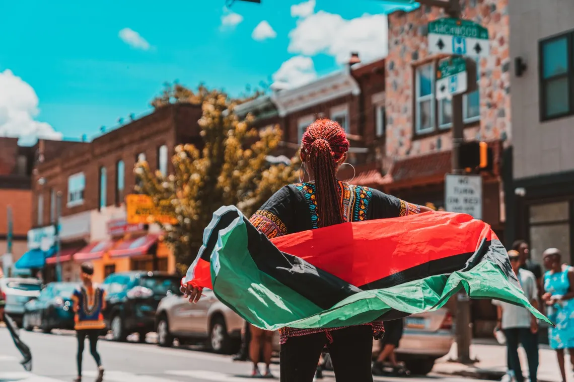 A small town street scene with a woman carrying a green, black and red flag