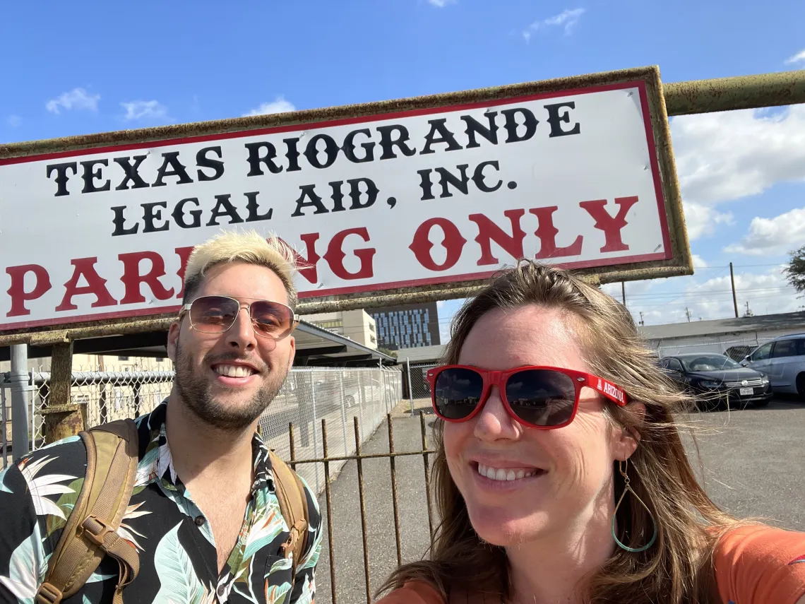 A man and woman stand smiling in front of a sign that reads Texas Rio Grande Legal Aid, Inc. Parking Only