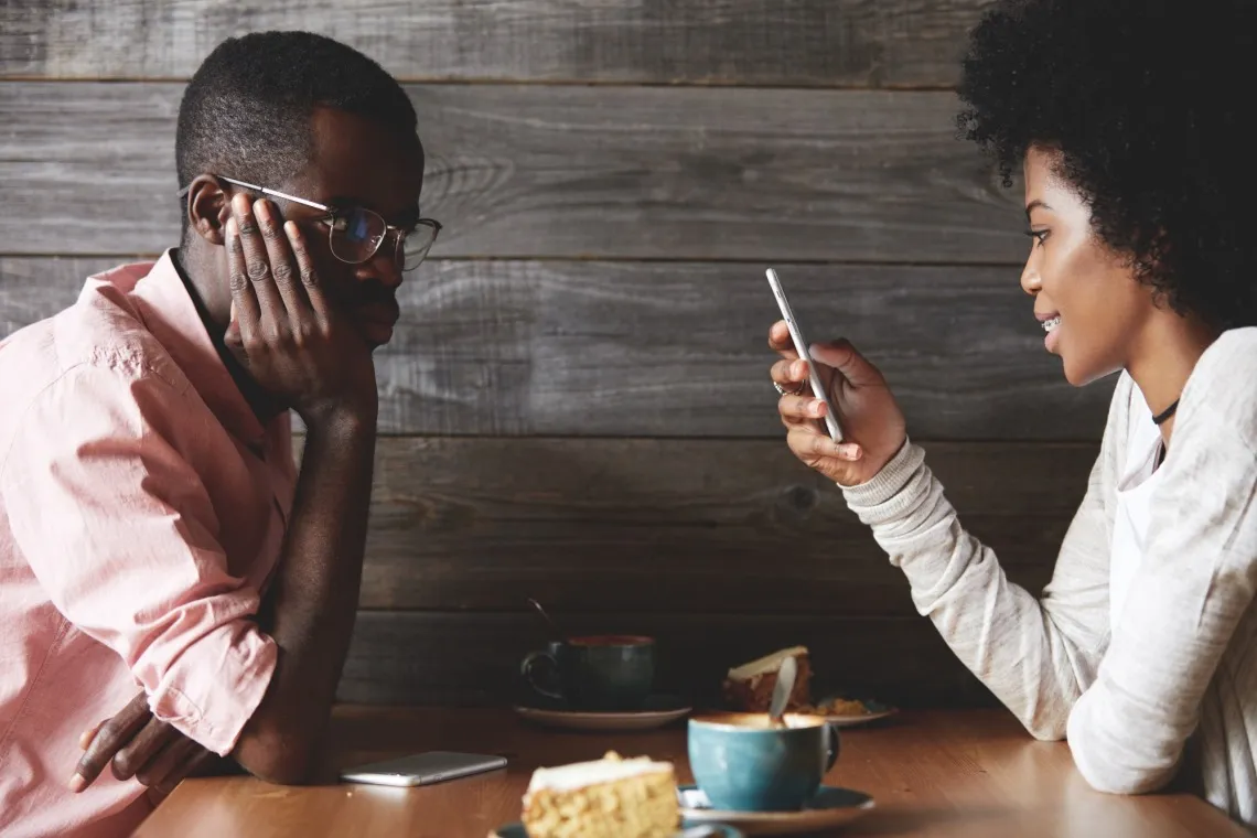 two people at table. one looking at smartphone