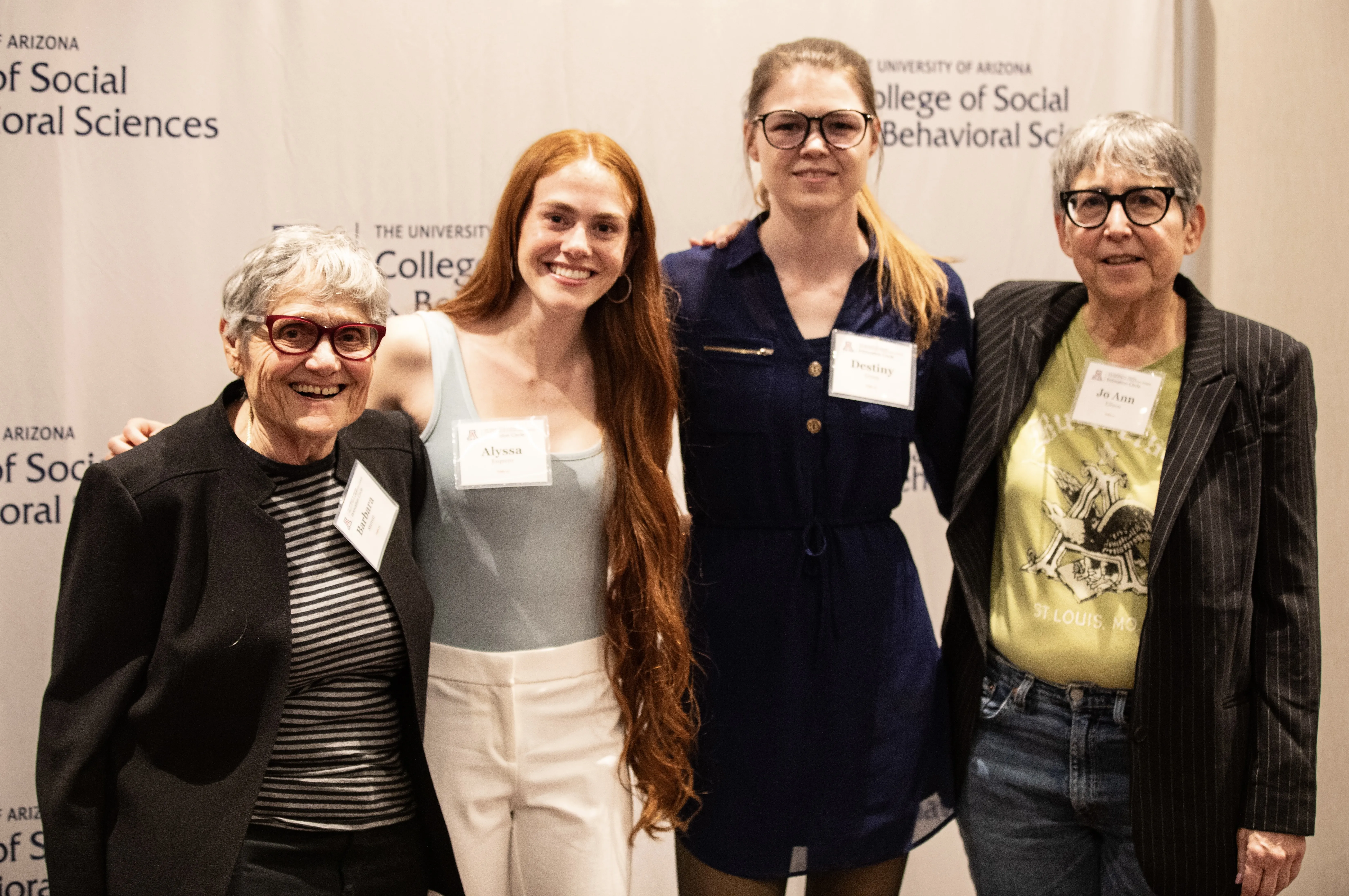 Two older women stand with two younger women, all posing in front of the SBS logo