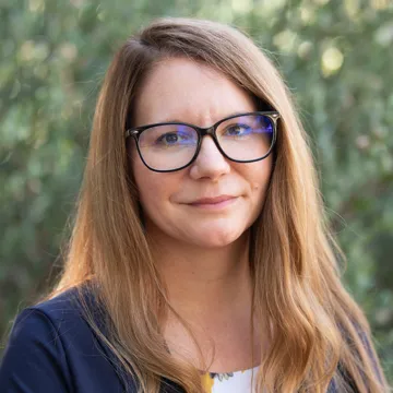 Woman with long light brown hair and glasses smiles while outside