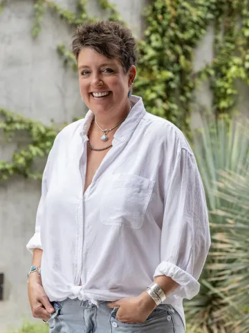 Woman with short hair and wearing a white blouse standing outside