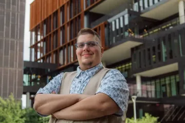 Student with glasses and vest stands outside in front of a building