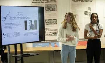 Lauren Hartwich (left) and Ziah Burks (right) stand in front of the class to present their project on a big screen TV