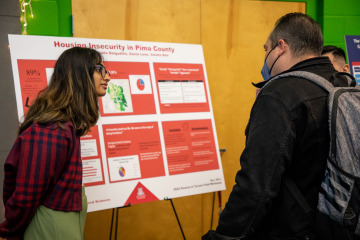 student listing to communty member in front of research poster