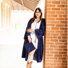 Woman with long brown hair standing outside in a graduation gown