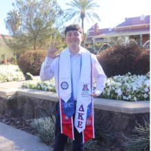 Man standing outside and waving hello, in a graduation gown