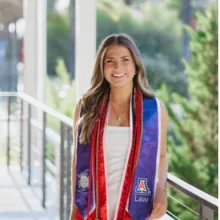 Woman with long blonde hair standing outside in graduation gown