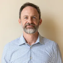 Man with beard and light blue shirt stands smiling