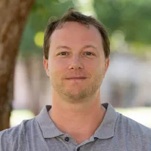 Man with short brown hair and a gray shirt standing outside