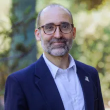 Man with glasses and blue sport coat stands outside