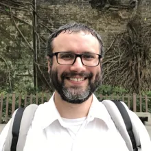 Man with a beard and glasses stands outside