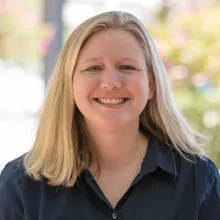 Blonde woman with navy blue shirt stands outside smiling