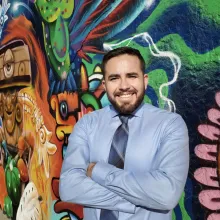 Man in blue shirt stands in front of a colorful mural