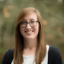 Woman with red hair and glasses stands outside