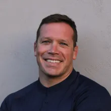 Man wearing a black shirt sits against a white wall