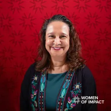 Woman with long brown curly hair sits in front of red background