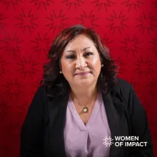 Woman with lavender blouse and black jacket sits in front of red background