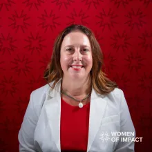 Woman with long brown hair and white jackets sits in front of a red background