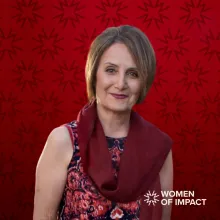 Woman with short light brown hair and a scarf sits in front of a red background