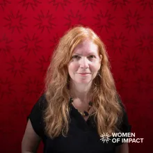 Woman with long red hair sits in front of a red background