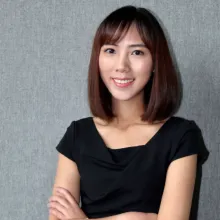 woman with black hair and black shirt stands against a grey background