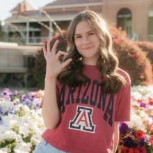 Anna Lineberry sits outside at a fountain, wearing a red Arizona shirt and showing the Arizona Wildcats sign