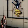 Student in Indigenous dress stands in front of an Indigenous piece of outdoor art