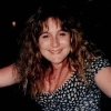 Woman with long curly hair and wearing a black and white flowered top smiles broadly