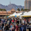 Crowd of people mill around white tents with mountains and palm trees in the background