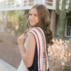 Student with long light brown hair and wearing graduation regalia stands outside in front of a cactus
