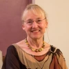 Mary Stiner sits in front of a brown and white wall, smiling
