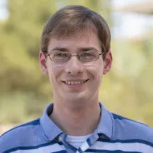 Man with blonde hair and glasses in a blue and white striped shirt