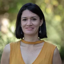 Woman with short black hair and wearing a yellow top stands outside