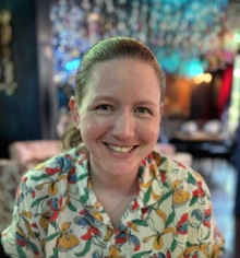 Woman with blonde hair, smiling and wearing a bright printed shirt