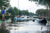 A street scene of flooding, with cars driving in deep water and a man in a canoe