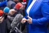 Woman in a blue suit and red nail polish stands in front of microphones